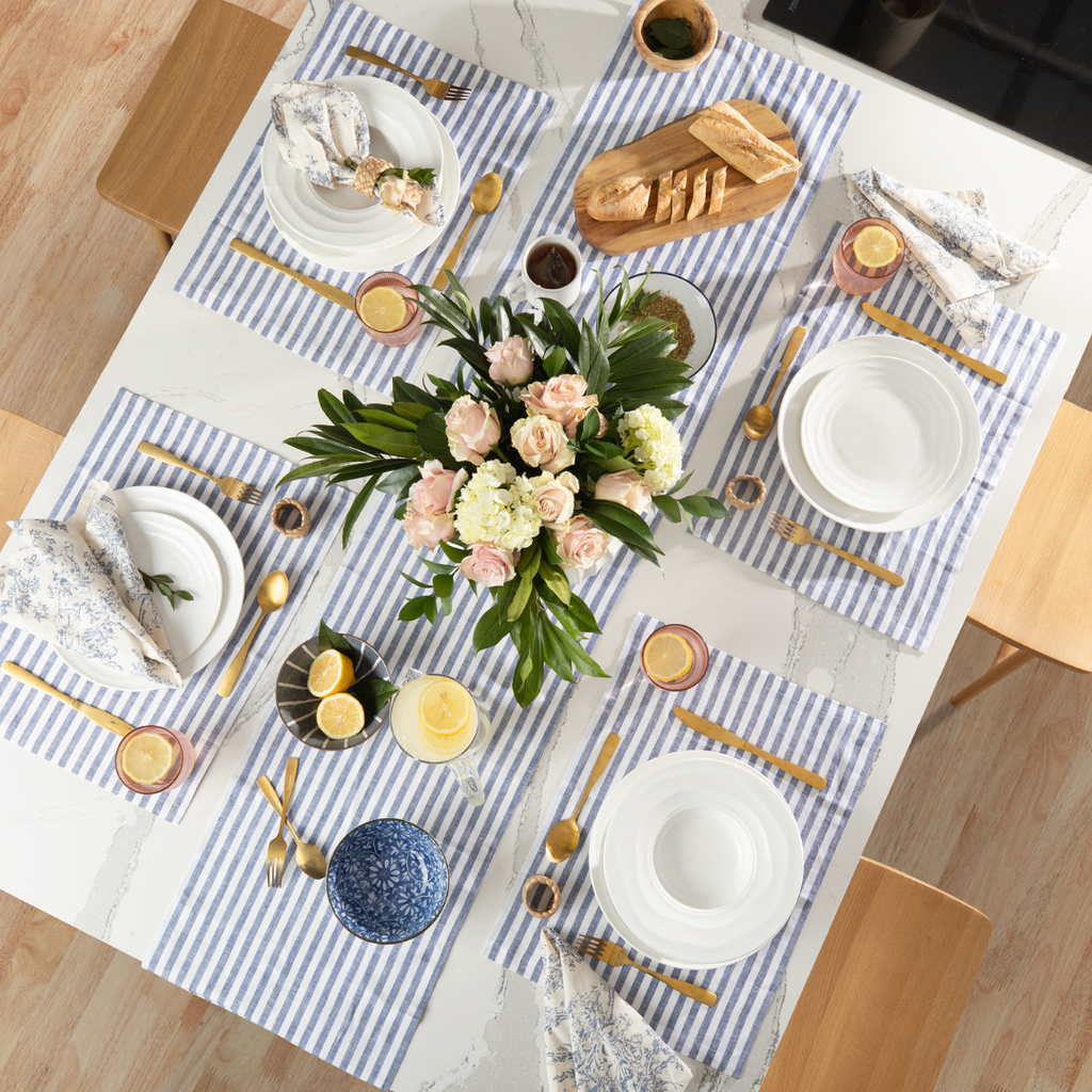 Elegant table setting with flowers, plates, and cutlery on a striped tablecloth.