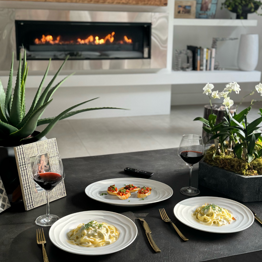 Dinner setting with plates of pasta, glasses of red wine, and a fireplace in the background.