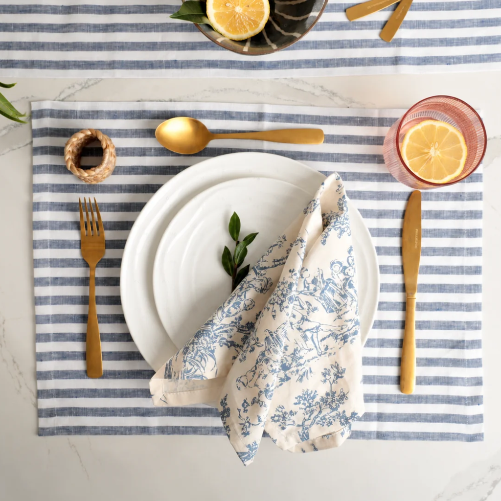 Natural Waves dinner plate place setting with a blue toile napkin, striped linen placemat and lemon water