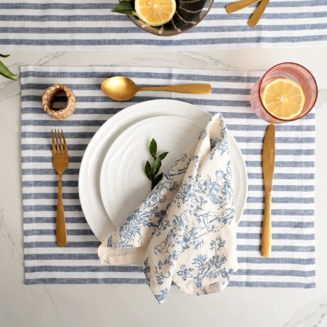 Natural Waves dinner plate place setting with a blue toile napkin, striped linen placemat and lemon water